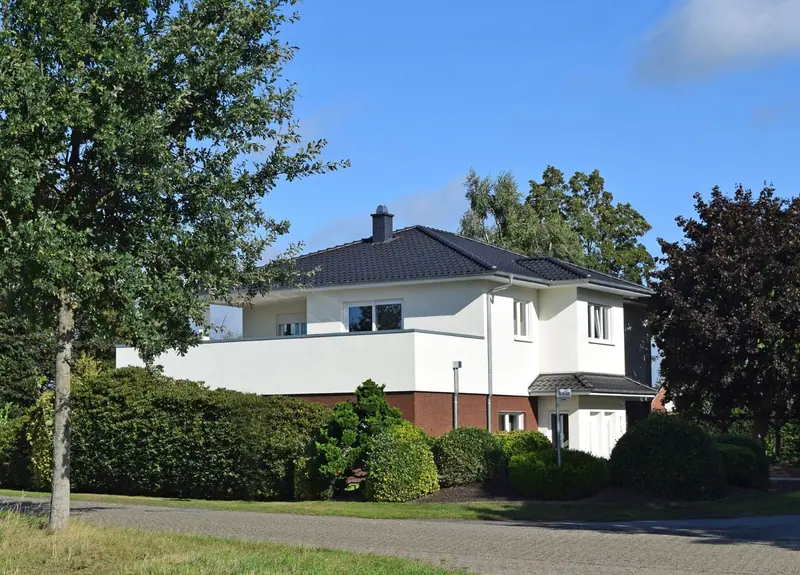 Weißes Einfamilienhaus mit Walmdach und Balkon